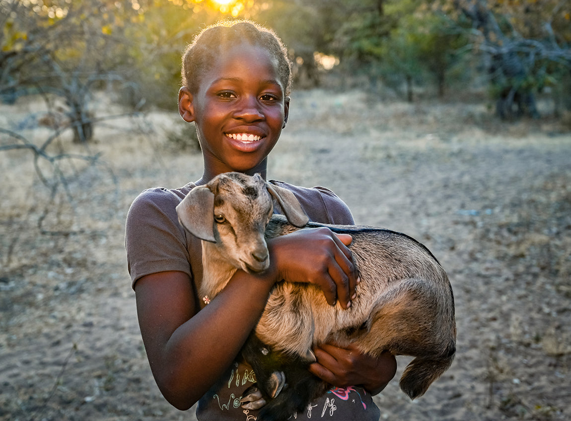 一個微笑著的女孩子，在室外手抱一隻山羊。