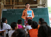  一名女士站在黑板前，手裡拿著一本書，展示給課室內的孩子們看。
