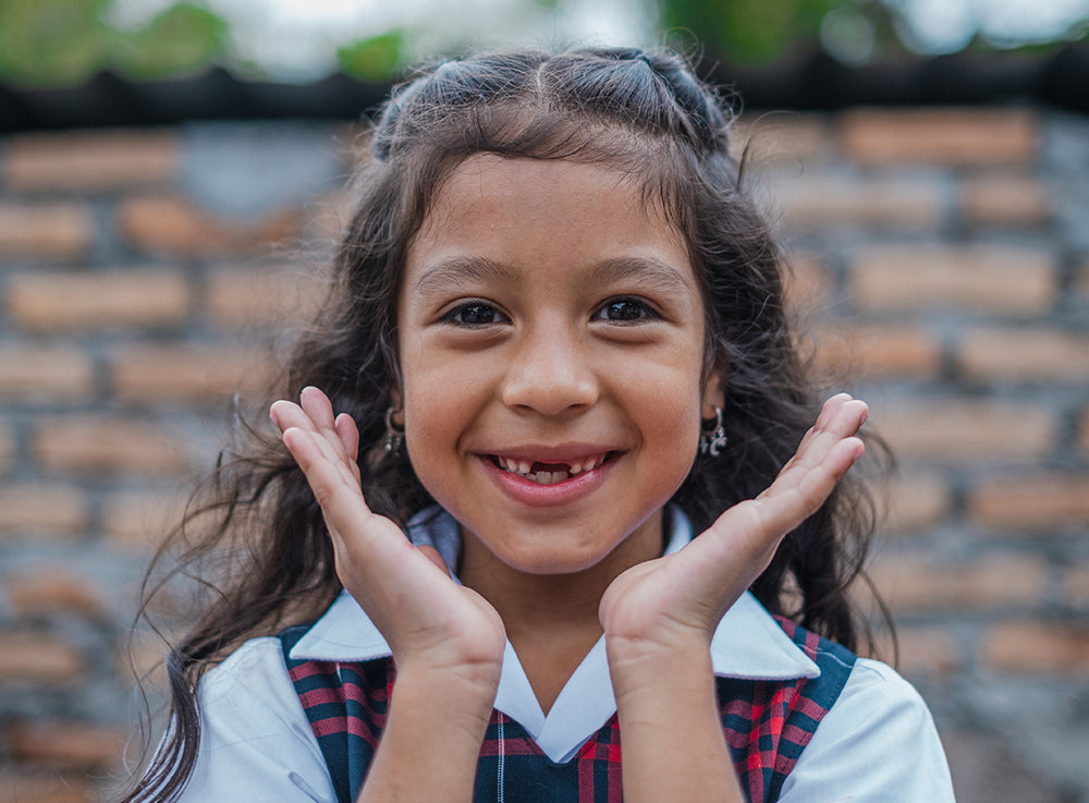  一名女童對著鏡頭微笑，雙手框住自己的臉。