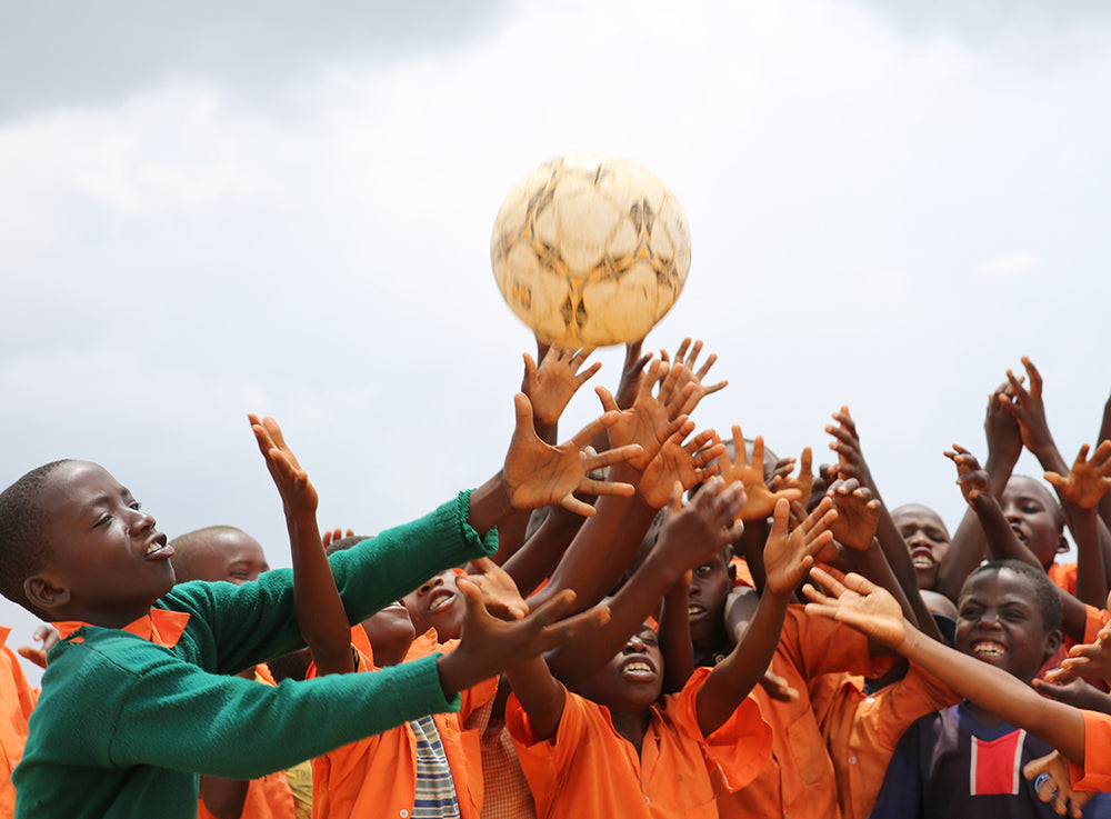  一大班小孩子伸手向著空中的足球。