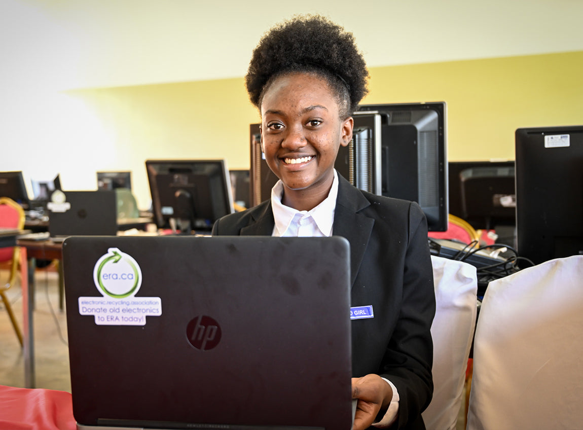 一個女孩子坐在電腦室內，面前放著一台手提電腦，並且對著鏡頭微笑。