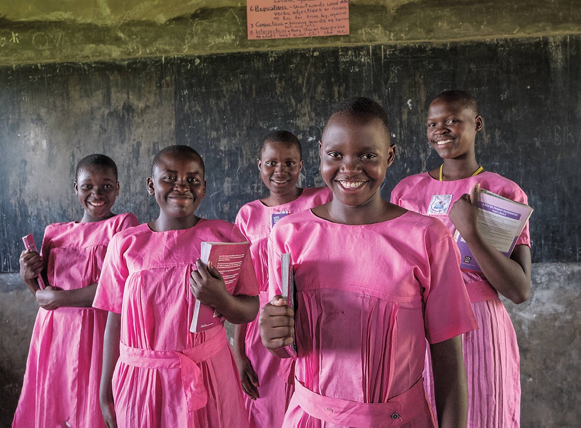 五個身穿粉紅色校服的女孩子，站在黑板面前，各自在懷裡拿著一本書。