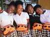 四個女童身穿格子校服裙，向著鏡頭微笑。她們手裡都拿著用小旅行袋裝著的衛生包。