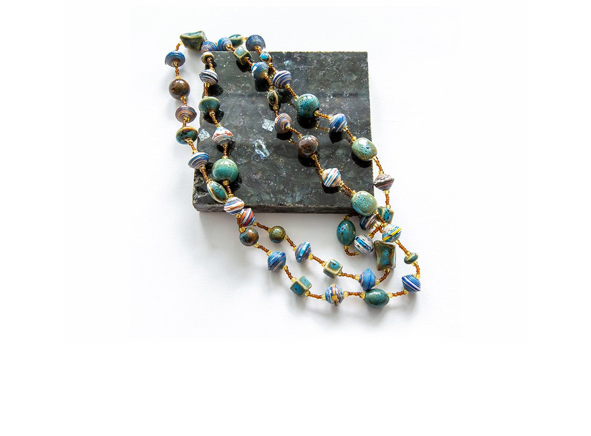 一條用不同形狀、顏色、大小的珠子製成的長項鏈，被放置在一塊方形石板上，以比對其大小比例。